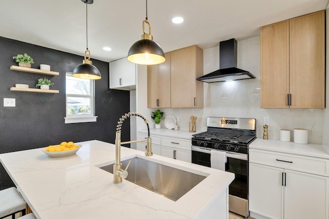 kitchen with light stone countertops, stainless steel range with gas cooktop, a sink, pendant lighting, and wall chimney exhaust hood