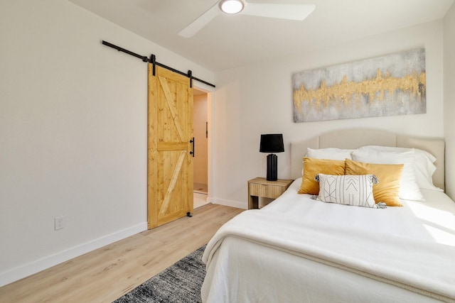bedroom with a ceiling fan, a barn door, wood finished floors, and baseboards