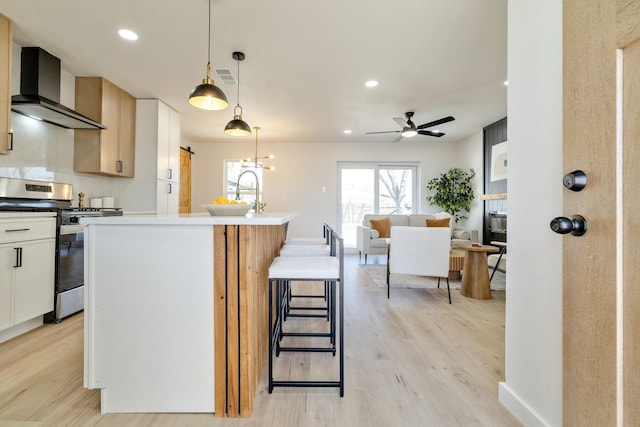 kitchen with light wood-type flooring, visible vents, wall chimney range hood, ceiling fan, and stainless steel gas range
