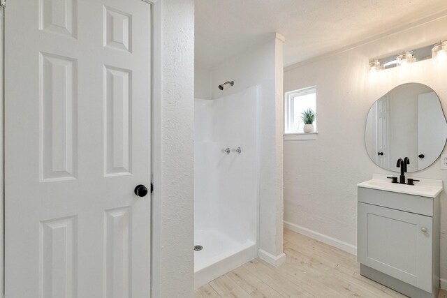 bathroom with baseboards, walk in shower, wood finished floors, and vanity