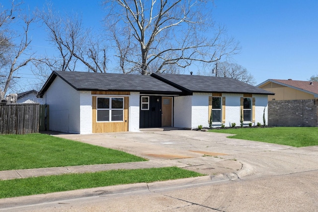 mid-century home with brick siding, driveway, a front lawn, and fence