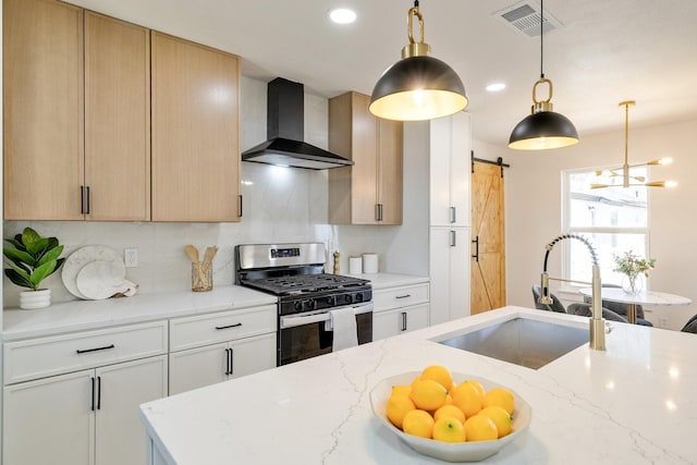 kitchen with stainless steel gas range, a sink, a barn door, wall chimney range hood, and backsplash