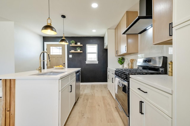 kitchen featuring a center island with sink, light wood-style flooring, a sink, appliances with stainless steel finishes, and wall chimney range hood