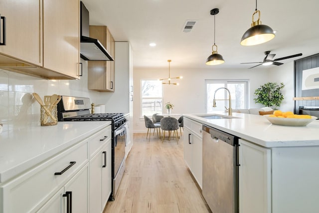 kitchen featuring visible vents, wall chimney range hood, appliances with stainless steel finishes, a ceiling fan, and a sink