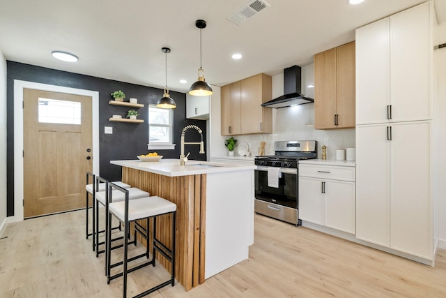 kitchen with stainless steel gas range oven, visible vents, a sink, wall chimney exhaust hood, and light countertops