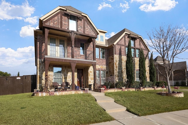 view of front of house with a front yard, a balcony, brick siding, and stone siding