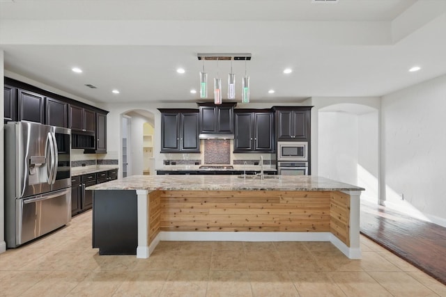 kitchen with a sink, tasteful backsplash, arched walkways, appliances with stainless steel finishes, and light tile patterned floors