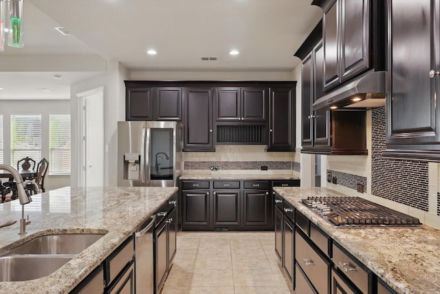 kitchen with light stone countertops, under cabinet range hood, decorative backsplash, appliances with stainless steel finishes, and a sink