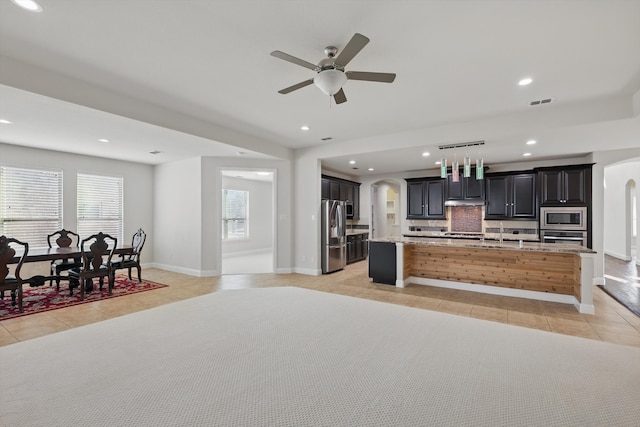 kitchen with a center island with sink, light tile patterned floors, arched walkways, and stainless steel appliances