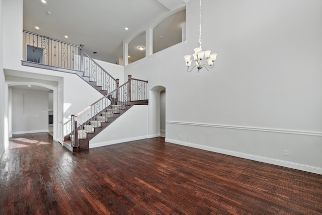 unfurnished living room featuring wood finished floors, stairway, arched walkways, an inviting chandelier, and a towering ceiling