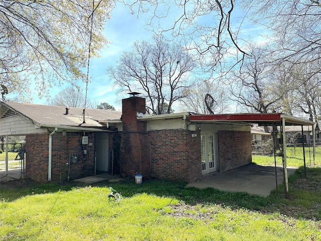 back of property featuring brick siding, an attached carport, fence, a chimney, and a yard