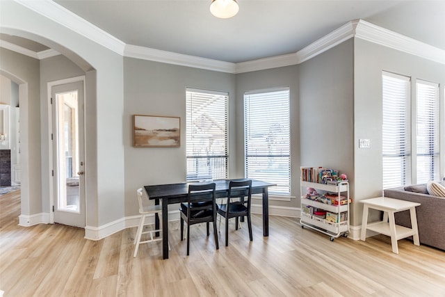dining area featuring crown molding, arched walkways, baseboards, and light wood finished floors