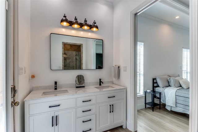 ensuite bathroom featuring crown molding, a healthy amount of sunlight, a sink, and wood finished floors