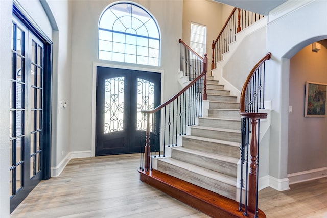 entrance foyer with stairs, arched walkways, french doors, and wood finished floors