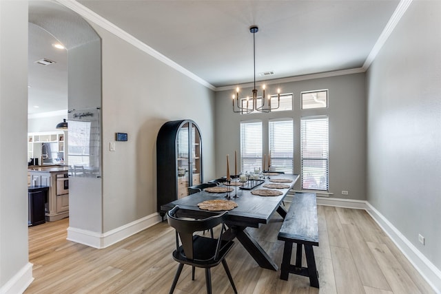 dining area featuring ornamental molding, baseboards, light wood-type flooring, arched walkways, and a notable chandelier