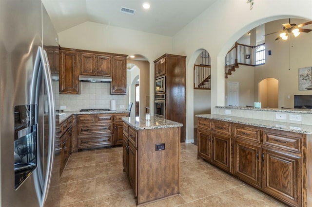 kitchen with under cabinet range hood, decorative backsplash, appliances with stainless steel finishes, arched walkways, and a ceiling fan