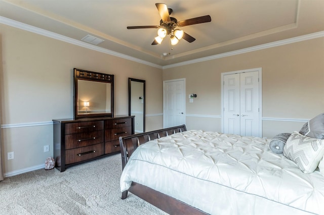 bedroom with ornamental molding, a tray ceiling, a closet, light colored carpet, and ceiling fan