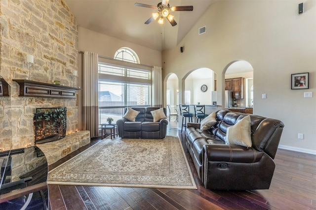 living room with a ceiling fan, visible vents, baseboards, arched walkways, and dark wood-type flooring