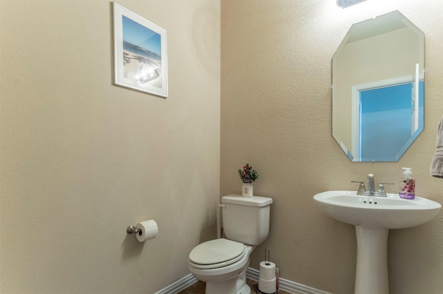 half bath featuring baseboards, toilet, and a textured wall