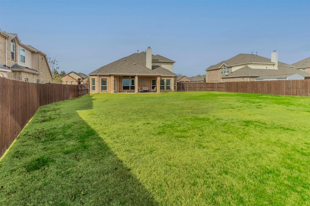 rear view of property featuring a lawn, a chimney, and a fenced backyard