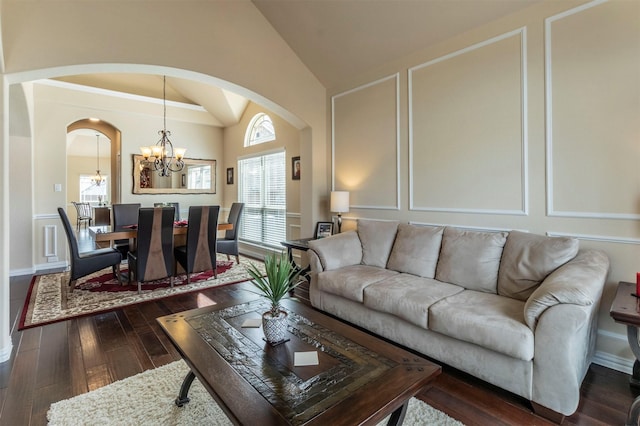 living area with arched walkways, a decorative wall, lofted ceiling, a chandelier, and dark wood-style flooring