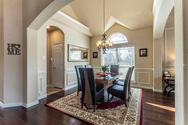 dining area with dark wood-type flooring, lofted ceiling, an inviting chandelier, arched walkways, and a decorative wall