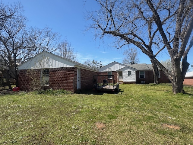 view of side of home featuring brick siding, a deck, and a yard