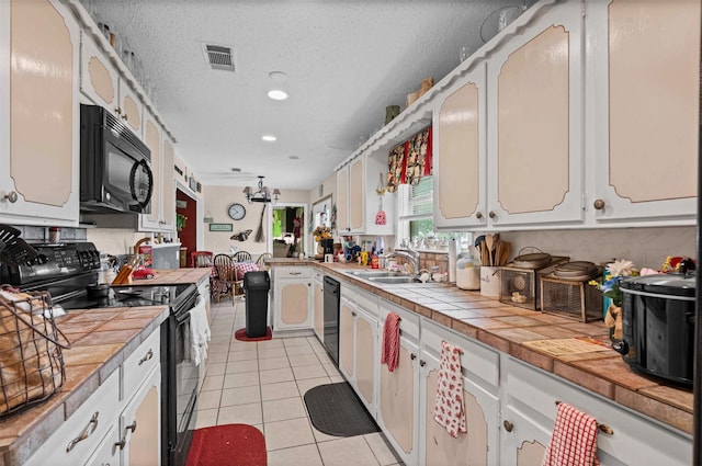 kitchen featuring tile countertops, visible vents, black appliances, and a sink