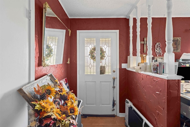 doorway with a textured ceiling, ornamental molding, and light wood-style floors
