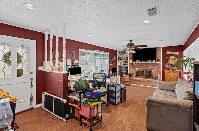 living area with hardwood / wood-style floors, a textured ceiling, visible vents, a fireplace, and a ceiling fan