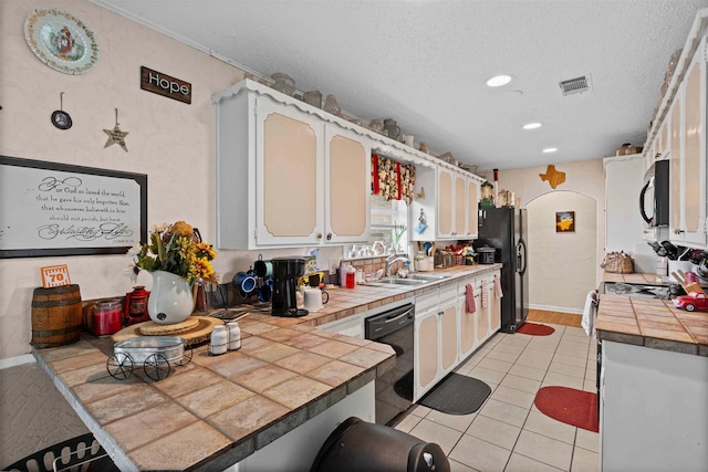 kitchen with a sink, light tile patterned flooring, tile countertops, black appliances, and visible vents