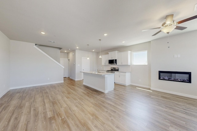 unfurnished living room with baseboards, light wood-type flooring, a ceiling fan, and recessed lighting