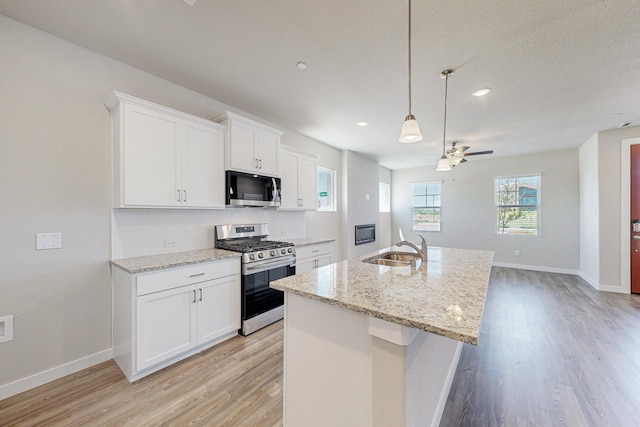 kitchen featuring a ceiling fan, appliances with stainless steel finishes, light wood finished floors, and a sink