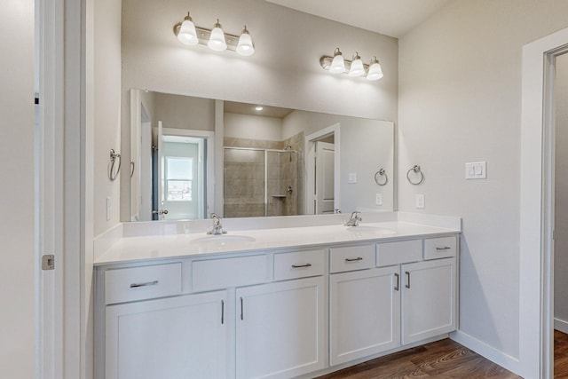 full bathroom with a stall shower, double vanity, a sink, and wood finished floors