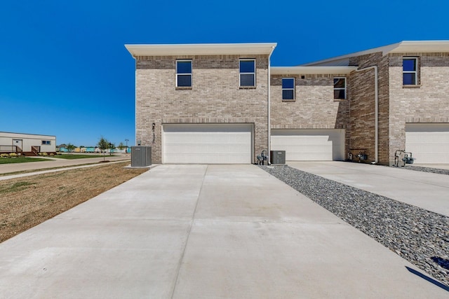 view of front of home with brick siding, central AC unit, concrete driveway, and an attached garage
