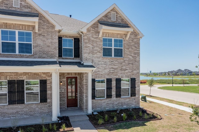 craftsman-style home featuring brick siding, a water view, and roof with shingles