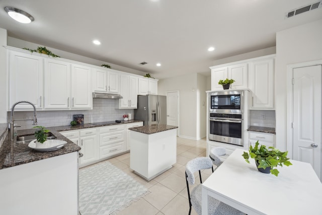 kitchen featuring visible vents, under cabinet range hood, light tile patterned floors, stainless steel appliances, and a sink