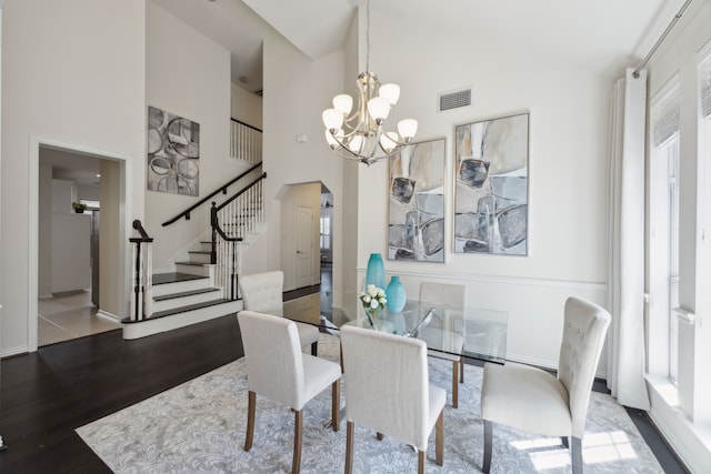 dining area with visible vents, wood finished floors, arched walkways, an inviting chandelier, and stairs