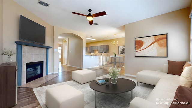 living area featuring visible vents, wood finished floors, ceiling fan, a tile fireplace, and arched walkways