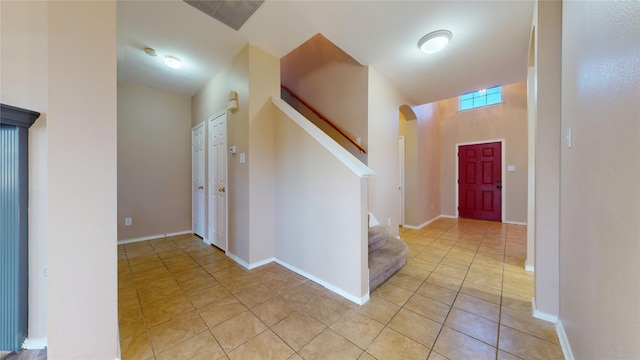 entrance foyer featuring baseboards, arched walkways, light tile patterned floors, and stairway