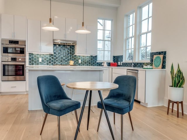 kitchen featuring under cabinet range hood, decorative light fixtures, decorative backsplash, appliances with stainless steel finishes, and white cabinetry