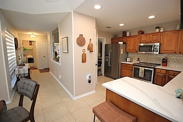 510 Canary Ln, Red Oak, TX 75154 - kitchen featuring appliances with stainless steel finishes, brown cabinetry, backsplash, light tile patterned floors, and baseboards