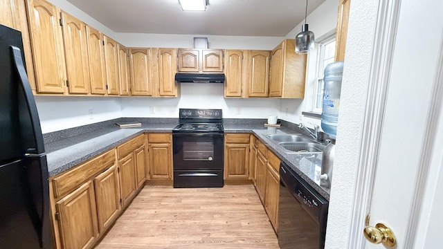 kitchen with under cabinet range hood, a sink, dark countertops, light wood-style floors, and black appliances