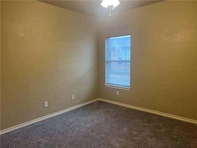 spare room with dark colored carpet, baseboards, and a ceiling fan