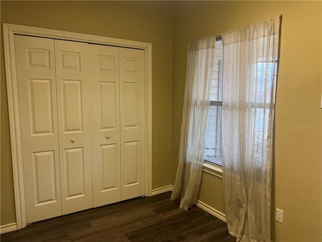 unfurnished bedroom featuring a closet, baseboards, and dark wood finished floors