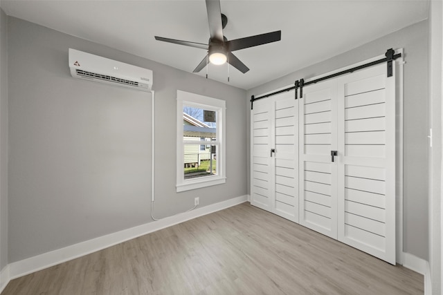 unfurnished bedroom featuring baseboards, wood finished floors, a wall unit AC, and a barn door