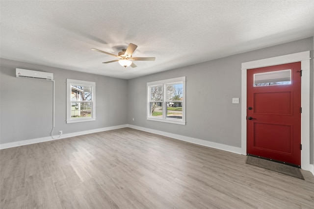 foyer entrance with an AC wall unit, a textured ceiling, light wood-type flooring, baseboards, and a ceiling fan