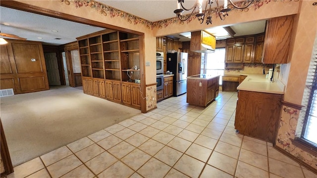 kitchen with light carpet, a notable chandelier, brown cabinets, a center island, and stainless steel appliances