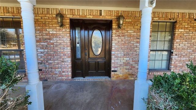 view of exterior entry featuring a porch and brick siding