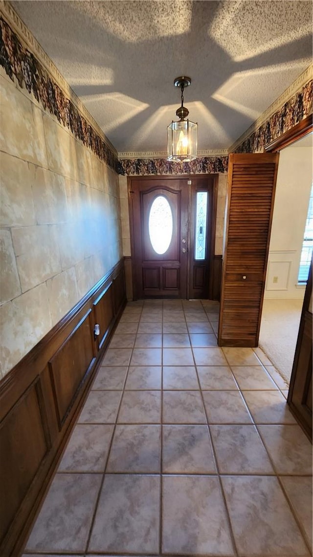 foyer entrance with light tile patterned flooring, wainscoting, and a textured ceiling